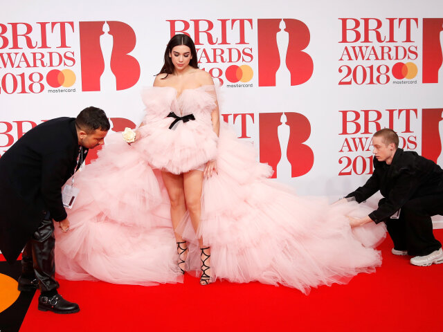 Asistenti pomáhajú speváčke Dua Lipa s jej masívnymi šatami. 