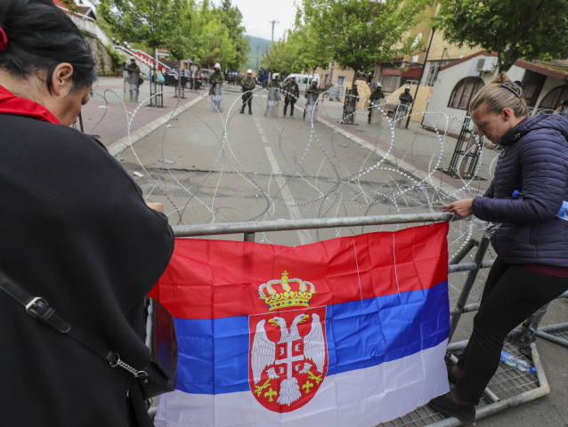Ženy upevňujú srbskú zástavu na oplotenie počas protestu pred budovou radnice po zrážkach polície s kosovskými Srbmi v obci Zvečan na severe Kosova 31. mája 2023