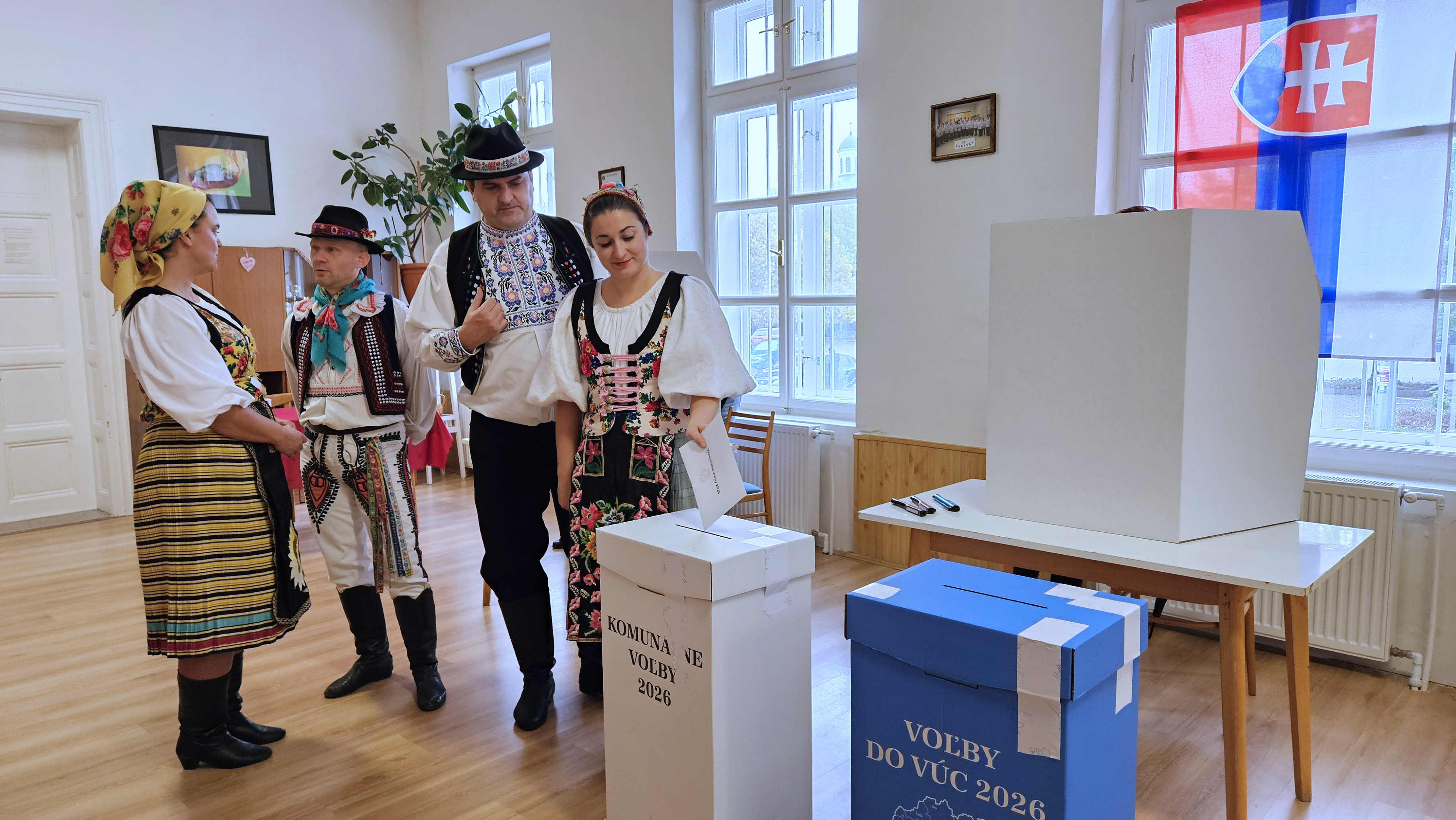 Na snímke volička s folklórneho súboru Slovenskí rebeli vhadzuje obálku s hlasovacími lístkami  do volebnej schránky pre komunálne voľby vo volebnej miestnosti v Komárne v sobotu 24. októbra 2026.